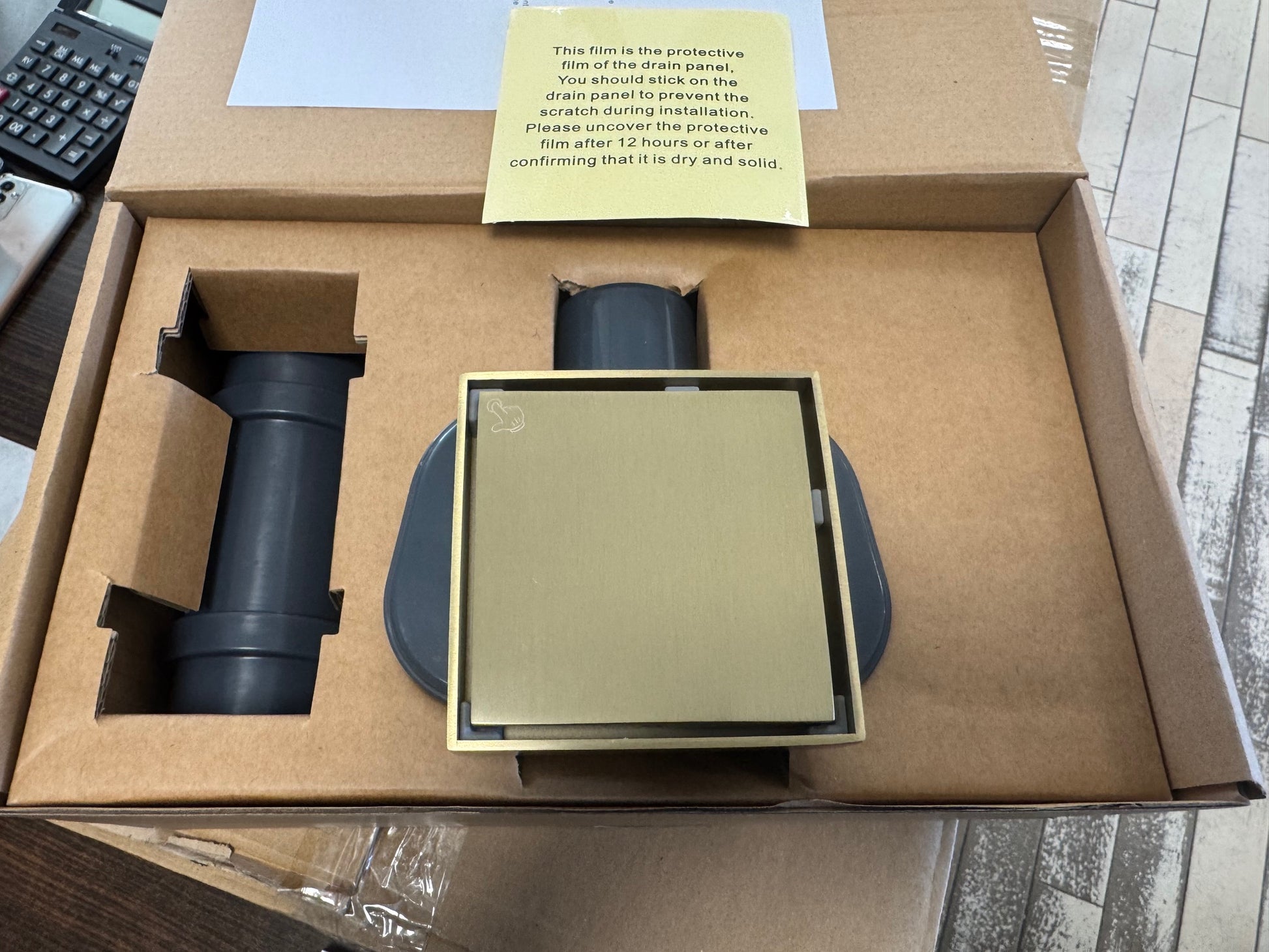 Подов сифон Velora Brushed Gold 10х10 см - драскано злато в опаковка с инсталационни инструкции.